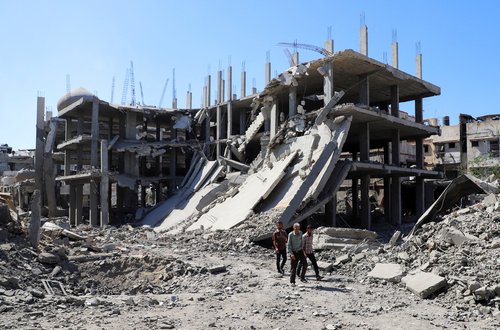 Palestinians walk past a destroyed building, as they inspect the damage in the aftermath of Israeli operation at Sabra neighbourhood in Gaza City, October 8, 2025.