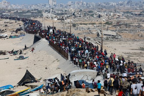 Palestinians, who were displaced to the southern part of Gaza at Israel's order during the war, make their way along a road past destroyed buildings as they return to the north after a ceasefire