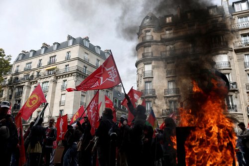 Protesters holding flags walk past a burning garbage bin during a demonstration in Paris as part of a day of nationwide strikes and protests against the government and possible austerity cuts in France