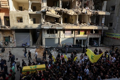 People walk past a damaged building during the funeral of Hezbollah's top military official, Haytham Ali Tabtabai, and of other people who were killed by an Israeli airstrike on Sunday