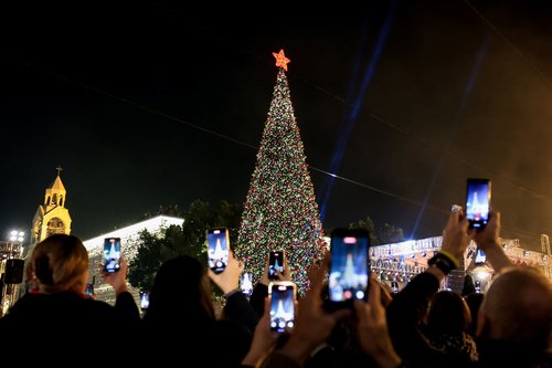 Palestinians use phones to record as a Christmas tree is lit up in Manger Square outside the Church of the Nativity, in Bethlehem, in the Israeli-occupied West Bank, December 6, 2025. REUTERS/Mussa Qawasma