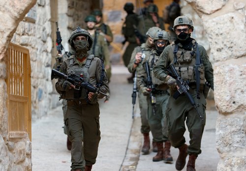 Israeli soldiers carrying weapons walk during a weekly settlers' tour in Hebron, in the Israeli-occupied West Bank
