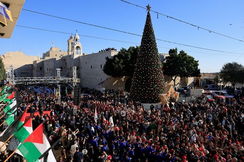 People gather next to the Christmas tree at Manger Square on the day of Christmas events with Cardinal Pierbattista Pizzaballa, Latin Patriarch of Jerusalem, on Christmas Eve