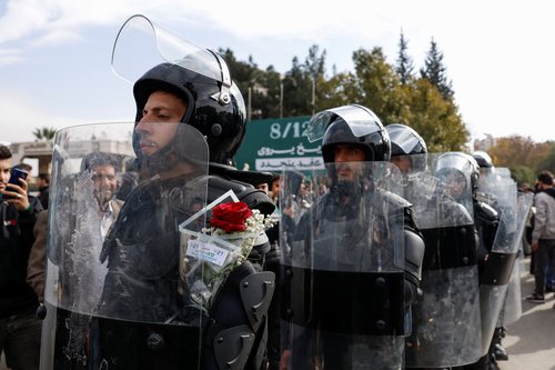 A Syrian police officer carries flowers behind his shield during the celebration of the first anniversary of Bashar al-Assad's fall, at Ummayad Square in Damascus, Syria, December 8, 2025.