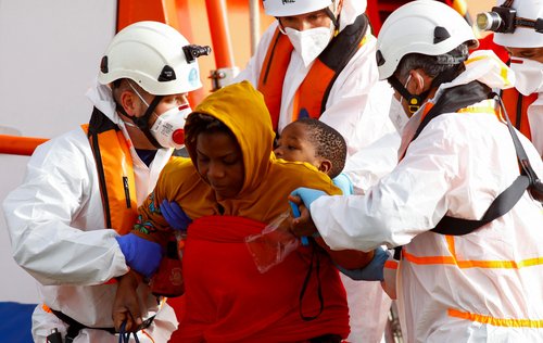 Rescuers help a migrant and her baby to disembark from a Spanish Coast Guard vessel, in the port of Arguineguin