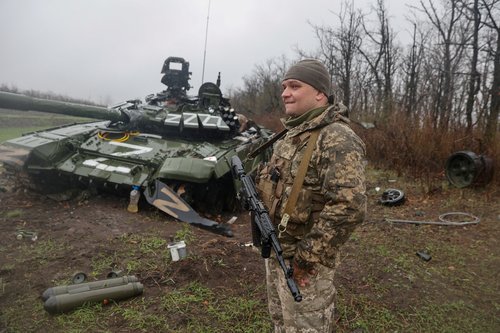 A Ukrainian service member stands next to a damaged Russian tank T-72 BV in Donetsk region