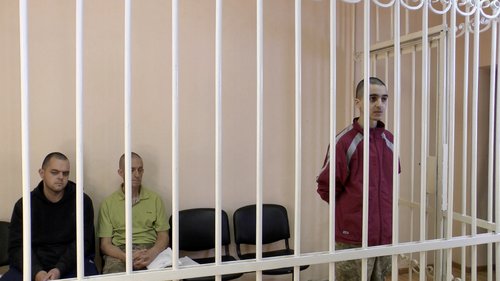 A still image shows Britons Aiden Aslin, Shaun Pinner and Moroccan Brahim Saadoun in a courtroom cage at a location given as Donetsk