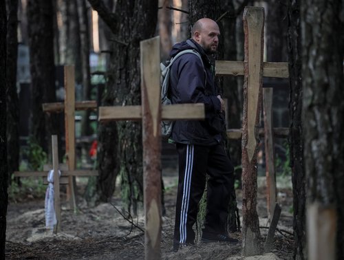 A local resident steppes between graves as he looks for relatives at a place of mass burial during an exhumation in the town of Izium