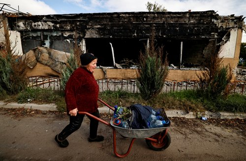 Galyna, 69, pushes her wheelbarrow besides a building, amid Russia's attack on Ukraine, in the newly recaptured town of Sviatohirsk