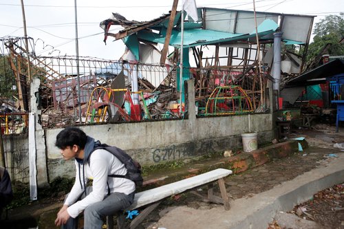 A man sits near a destroyed kindergarten affected by the earthquake in Cugenang