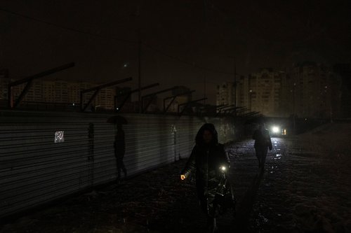 Women walk along a dark street after critical civil infrastructure was hit by Russian missile attacks in Kyiv