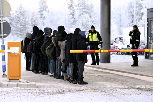 Migrants are lined up in front of Finnish Border Guards at the international border crossing at Salla