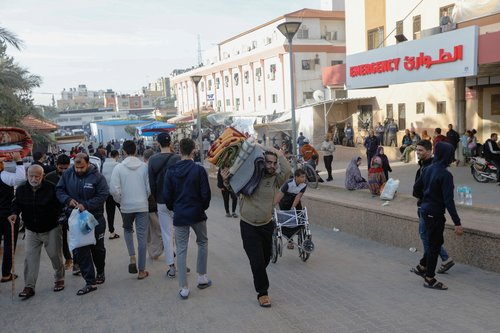 A displaced Palestinian man, who fled his house due to Israeli strikes, carries his belongings as he makes his way back to his home, in Khan Younis
