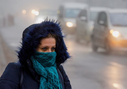 A woman wearing a mask walks as fog blankets the city of Skopje