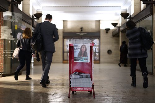 Commuters walk past copies of the Evening Standard at a subway station in London