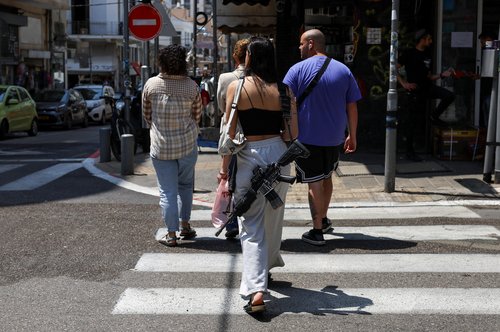 A woman carries a weapon as she walks, in Tel Aviv