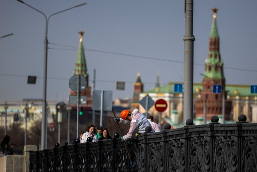 A communal worker paints a fence on a bridge in Moscow