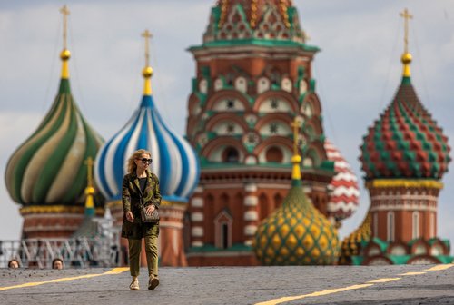 A woman walks in the Red Square with the domes of St. Basil's Cathedral in the background in Moscow