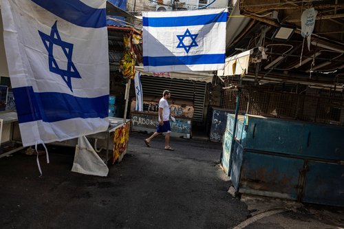 A man walks past Israeli flags at the green market, in Tel Aviv