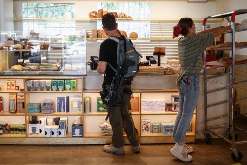 Israeli reservist carrying rifle orders at coffee shop in Tel Aviv