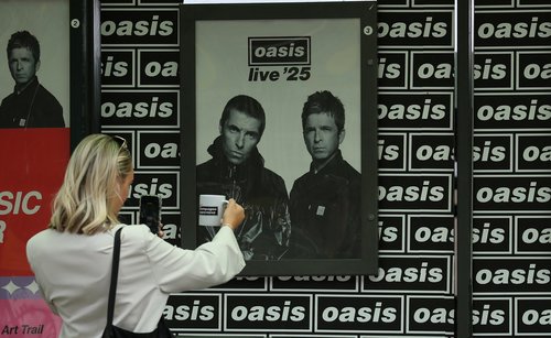 A woman takes photographs of a mug in front of Oasis posters ahead of their concerts in Heaton Park in Manchester, Britain, July 9, 2025. REUTERS/Phil Noble