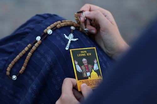 A woman holds a rosary and a card portraying Pope Leo outside Gemelli Hospital, where the Pontiff is being treated for lung cancer following surgery to remove part of his right lung, in Rome, Italy, October 14, 2026. REUTERS/Yara Nardi