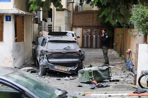 An Israeli police officer stands near a wrecked car at the site of damage, caused after Iran launched missiles towards Israel, amid the U.S.-Israel conflict with Iran, in Tel Aviv, Israel April 1, 2026