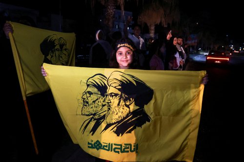 A girl holds a flag with an image depicting former Hezbollah leaders Hassan Nasrallah and Hashem Safieddine, as displaced people return to their homes after a 10-day ceasefire between Lebanon and Israel went into effect