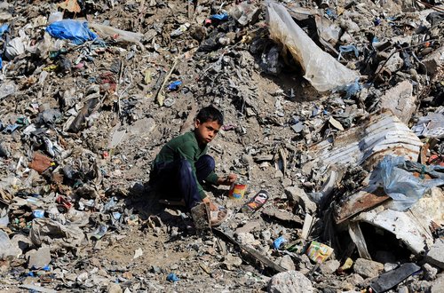 A Palestinian boy sits in a garbage dump near a cigarette market in Gaza City, April 20, 2026.