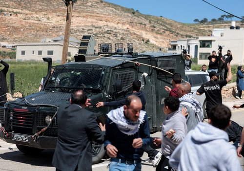 Mourners hurl stones at an Israeli military vehicle amid clashes during the funeral for two Palestinians killed after Israeli settlers and soldiers opened fire, according to witnesses