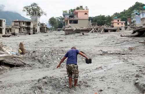 A man navigates through a mud-covered street next to damaged houses following the flash floods and mudslide, at Devighat, Nuwakot district, Nepal, August 29, 2026.