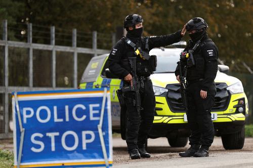 Armed police officers work on a road outside the perimeter of the RAF Fairford airbase, after police declared a major incident at the base after several men were arrested on suspicion of offences under the Explosives Act, in Fairford, Gloucestershire