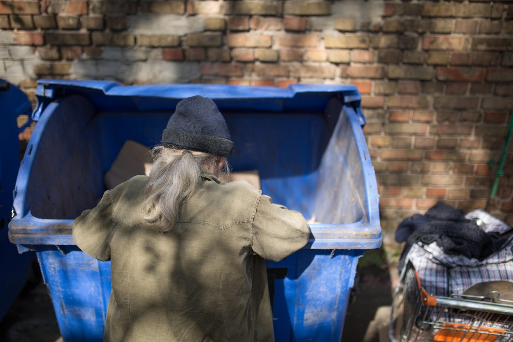 Homeless old man digging in trash can.