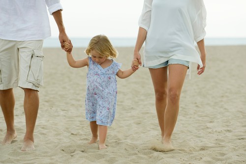 Little girl walking on beach with her parents, cropped