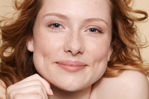 Studio shot of young woman with curly red hair, hand on chin