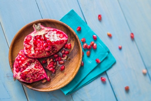 Overhead view of halved pomegranate on wooden plate