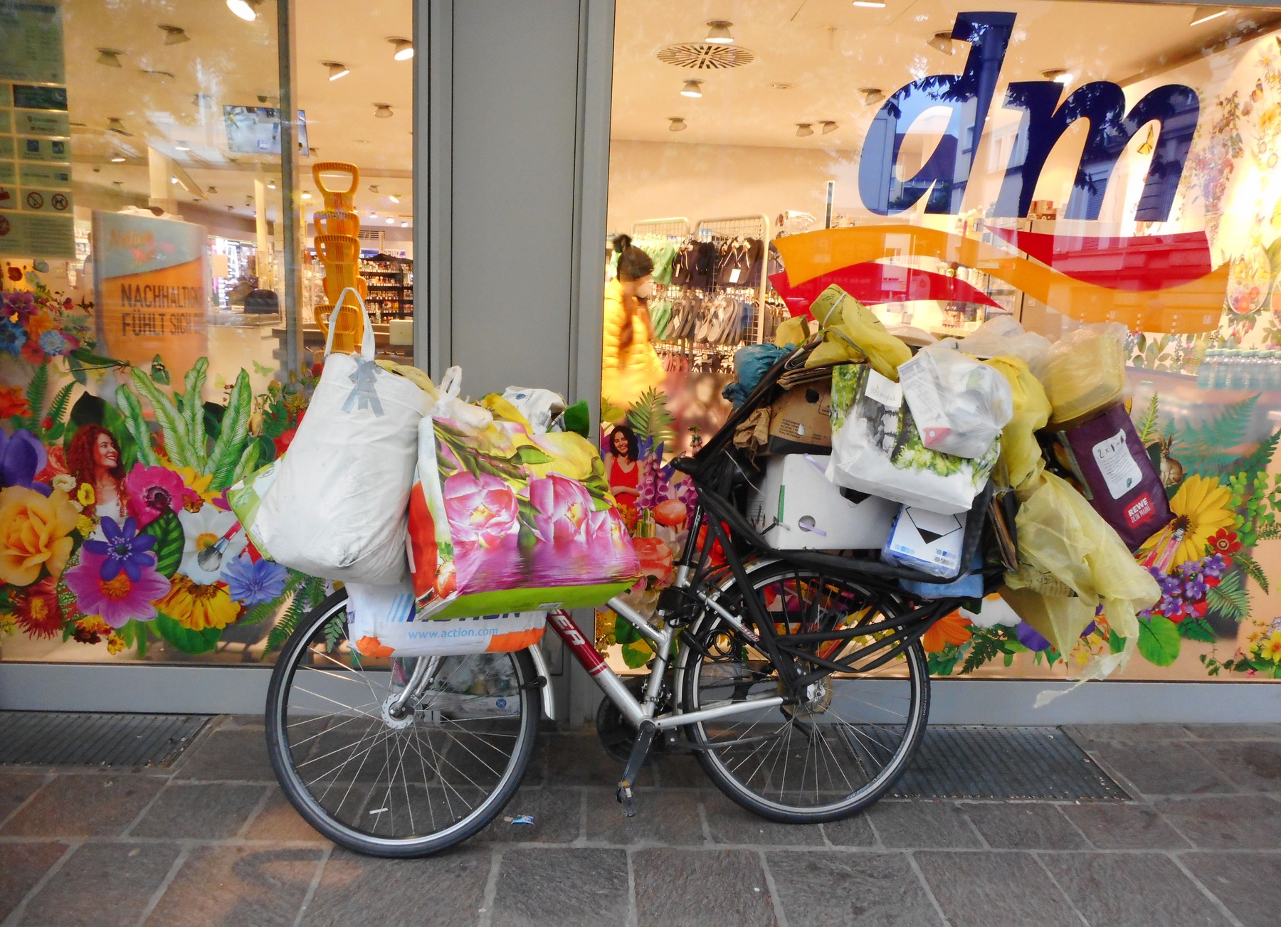 Germany, Freiburg: Bicycle overloaded with parcels and shopping bags parked on the shop window of a DM-drogerie market
