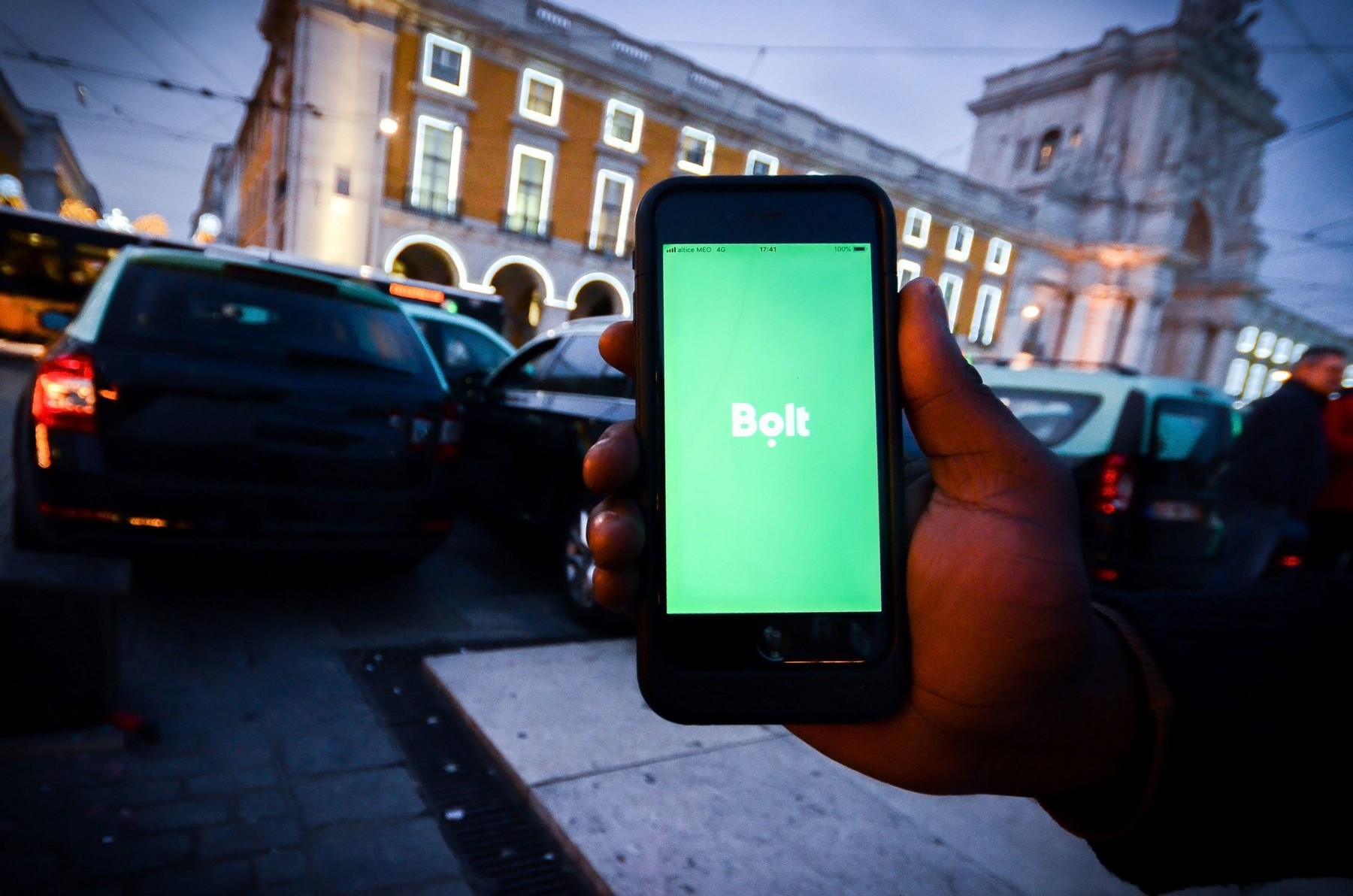 Lisbon, Portugal - Jan 3, 2010: Illustrative editorial of a man handholding a smartphone with a Bolt app in front of parked taxis. Bolt is smartphone