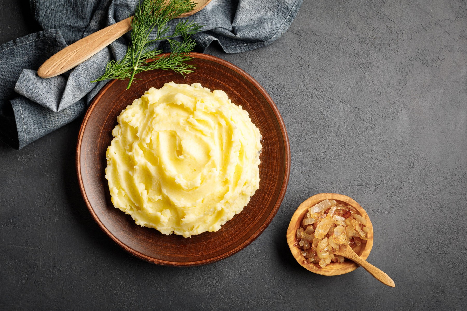 Mashed potatoes, boiled puree in a brown plate on a black slate background. Top view. Flat lay.