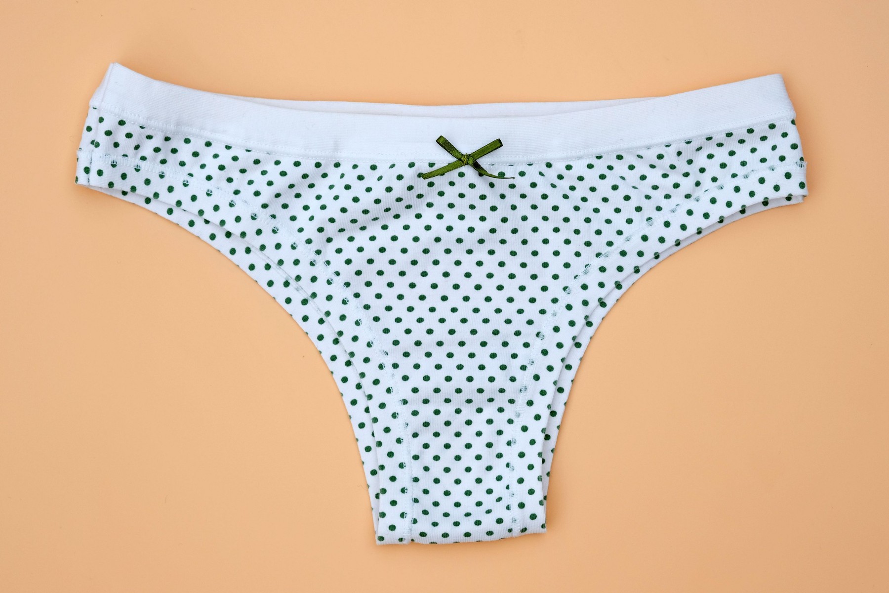 White cotton panties in green peas on a light brown background. Women's panties with a green bow top view. Cotton underwear.