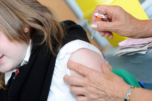 A school nurse injects a 12 year old school girl with the HPV vaccination to immunise against cervical cancer