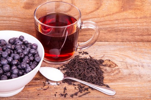 cup of tea and blueberry in white bowl on a wooden background