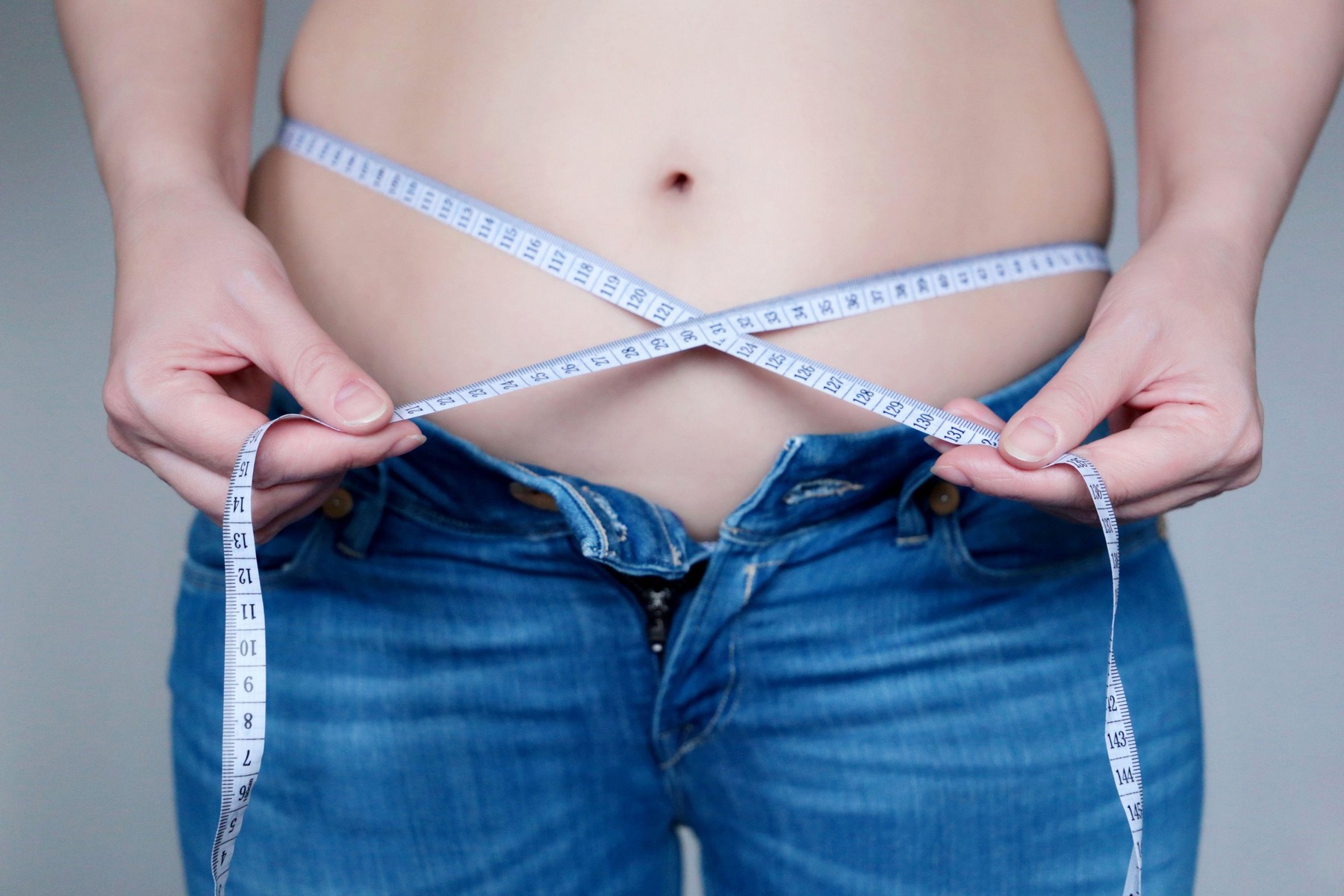 Overweight and overeating, female fat belly, woman in unbuttoned jeans with measuring tape around the waist. Obesity, weight loss, slimming and diet
