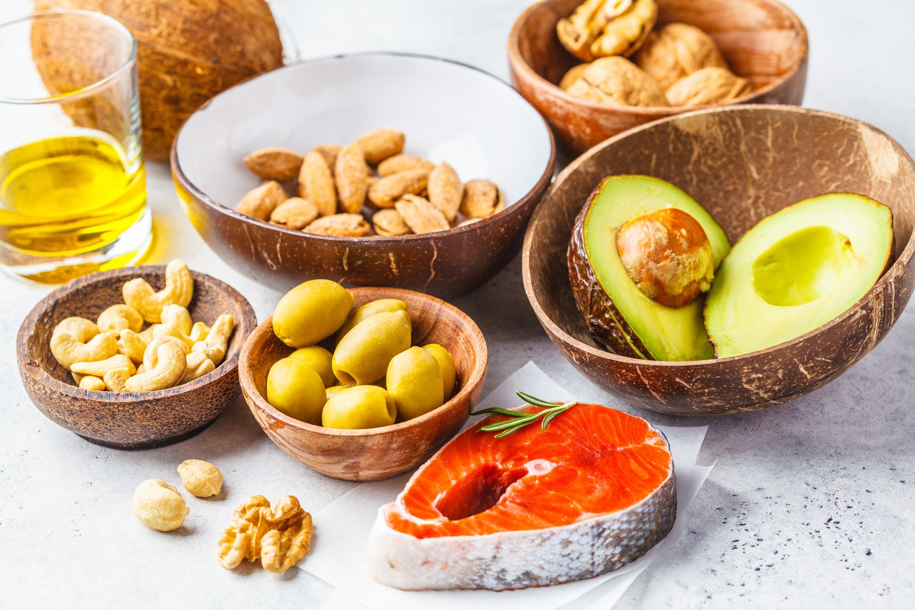 Selection of healthy fat sources: fish, nuts, oil, olives, avocado on white background.