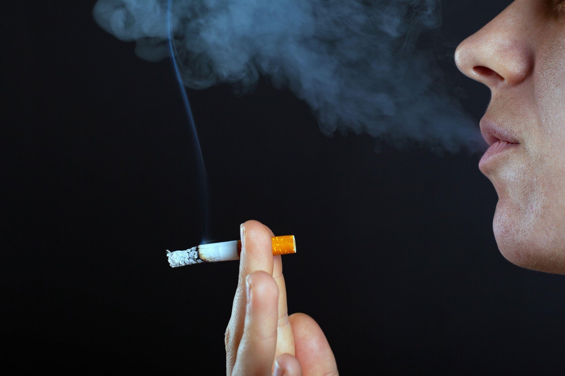 girl woman smokes a cigarette in white smoke on a dark background copy space.