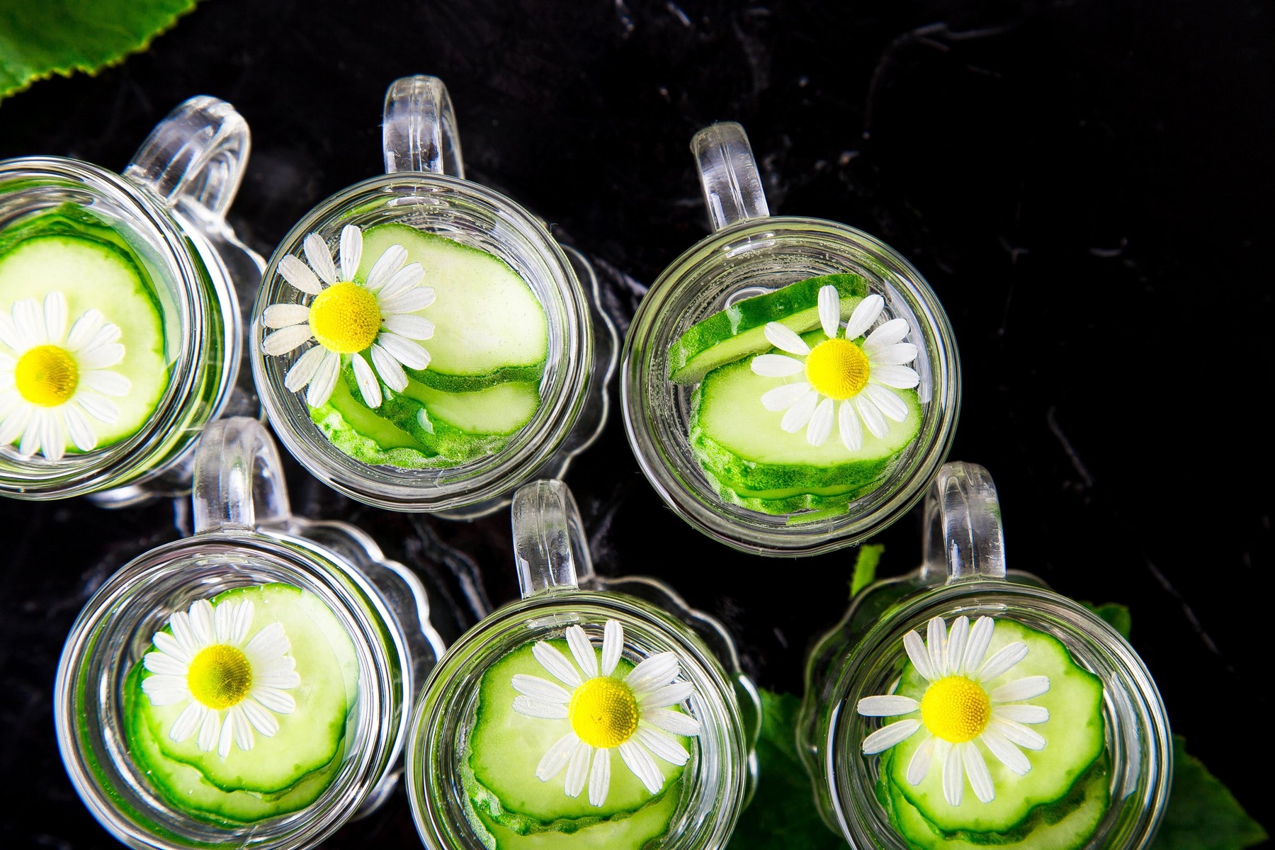 Cucumber water in six little mason glass jar on black background. Top view