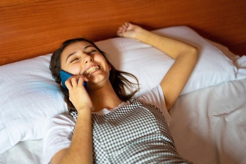 Woman lying in bed and talking on the phone. Laughing on a call. Talking to the family on the phone.