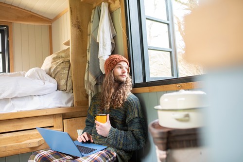 Young man with coffee using laptop in tiny cabin