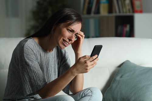 Sad woman at home checking smart phone in the night