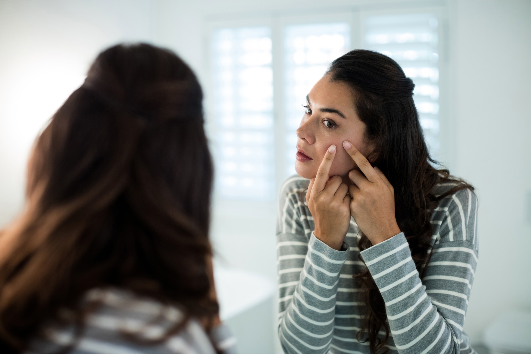 Woman squeezing pimples in front of bathroom mirror